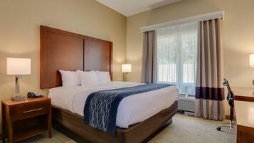 A hotel room with a large bed, two bedside lamps, a nightstand, a desk with a lamp, and a window with curtains.