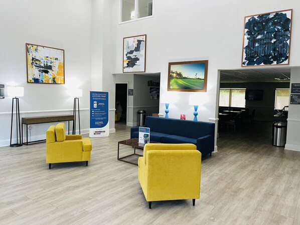 A hotel lobby with a reception desk, yellow armchairs, a blue sofa, and artwork on the walls.