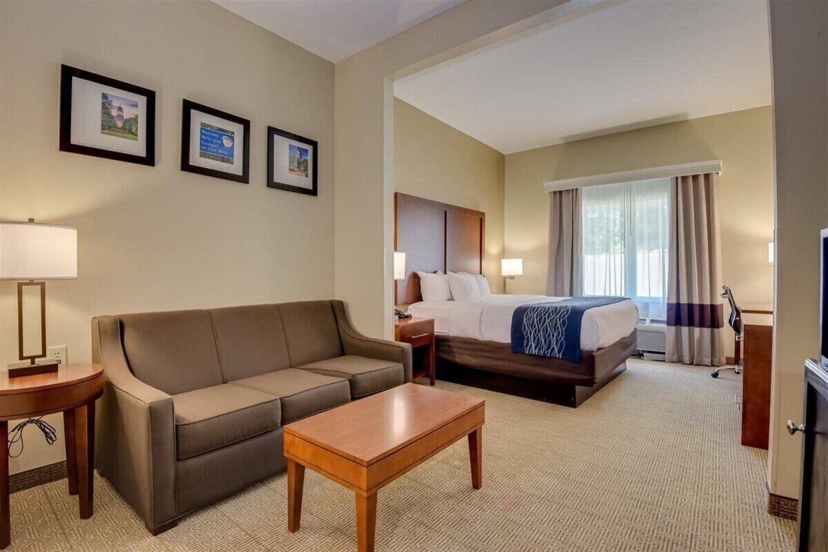 A hotel room with a sofa, a bed, a wooden coffee table, and framed pictures on the wall.