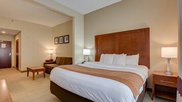 A hotel room with a large bed, a wooden headboard, a nightstand, a lamp, a small table, and a sofa.