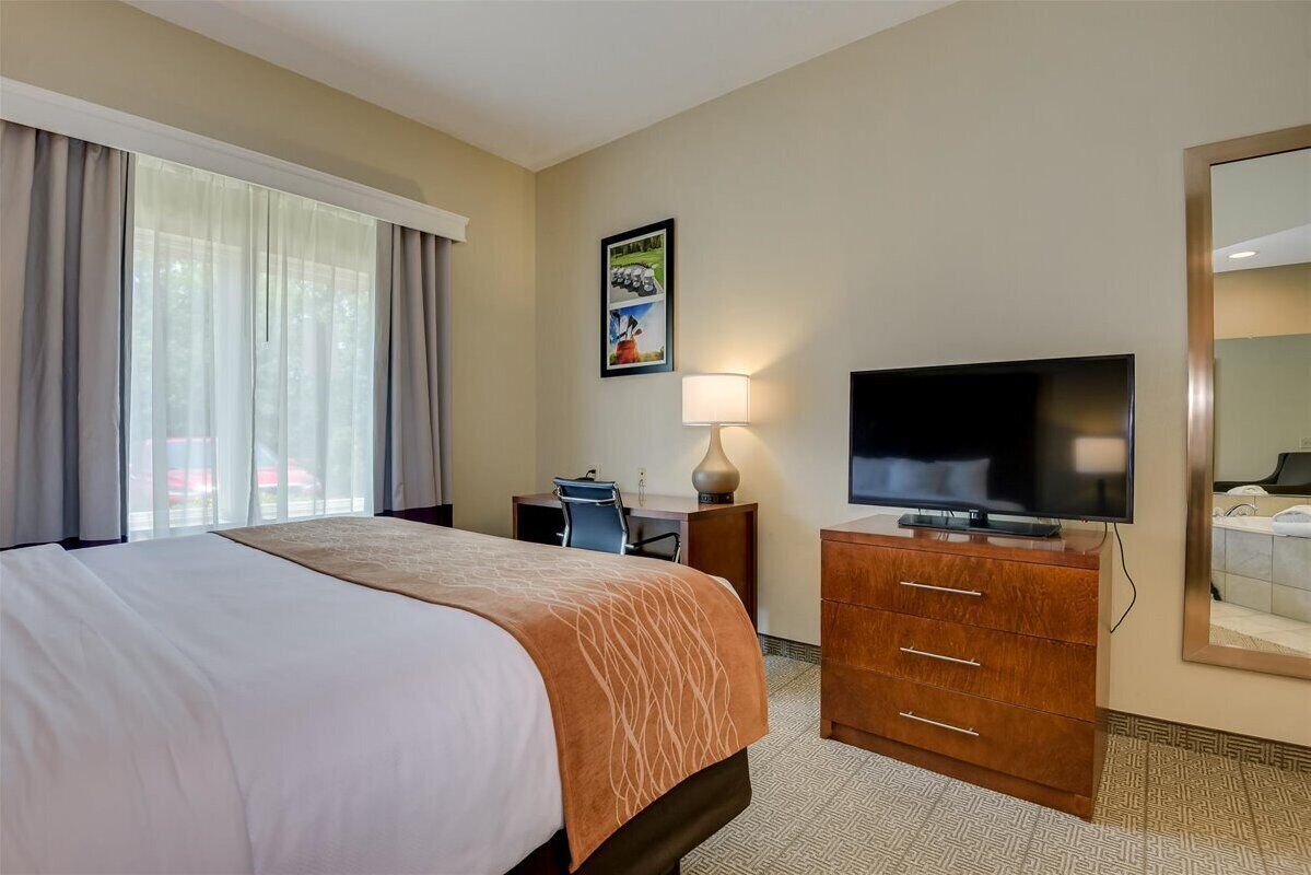 Una habitación de hotel con una cama grande, un escritorio con una silla, un televisor y un espejo.