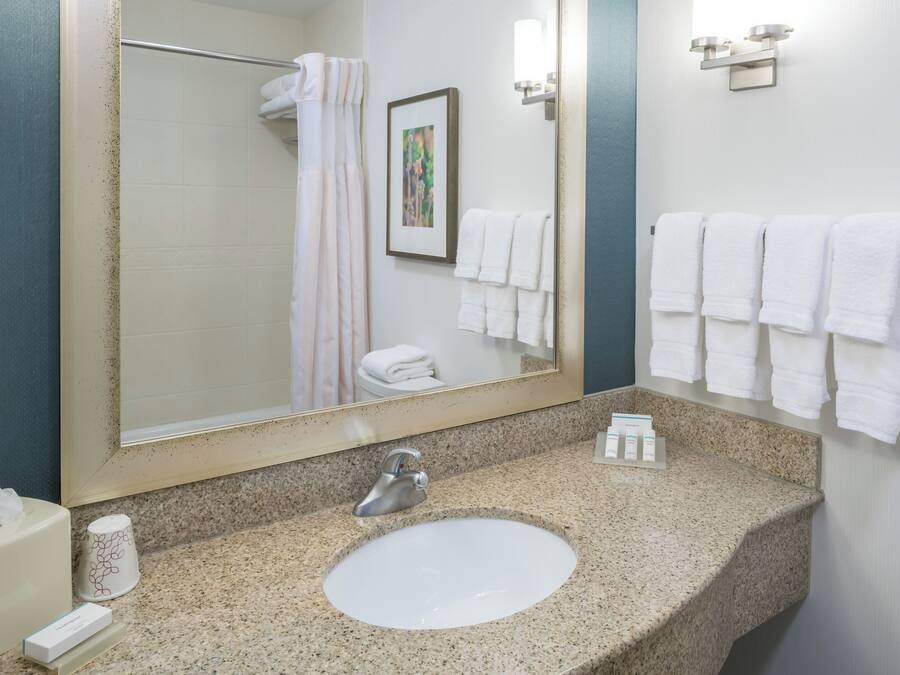 A bathroom with a granite countertop sink, a large mirror, a towel rack with multiple towels, and a framed picture on the wall.