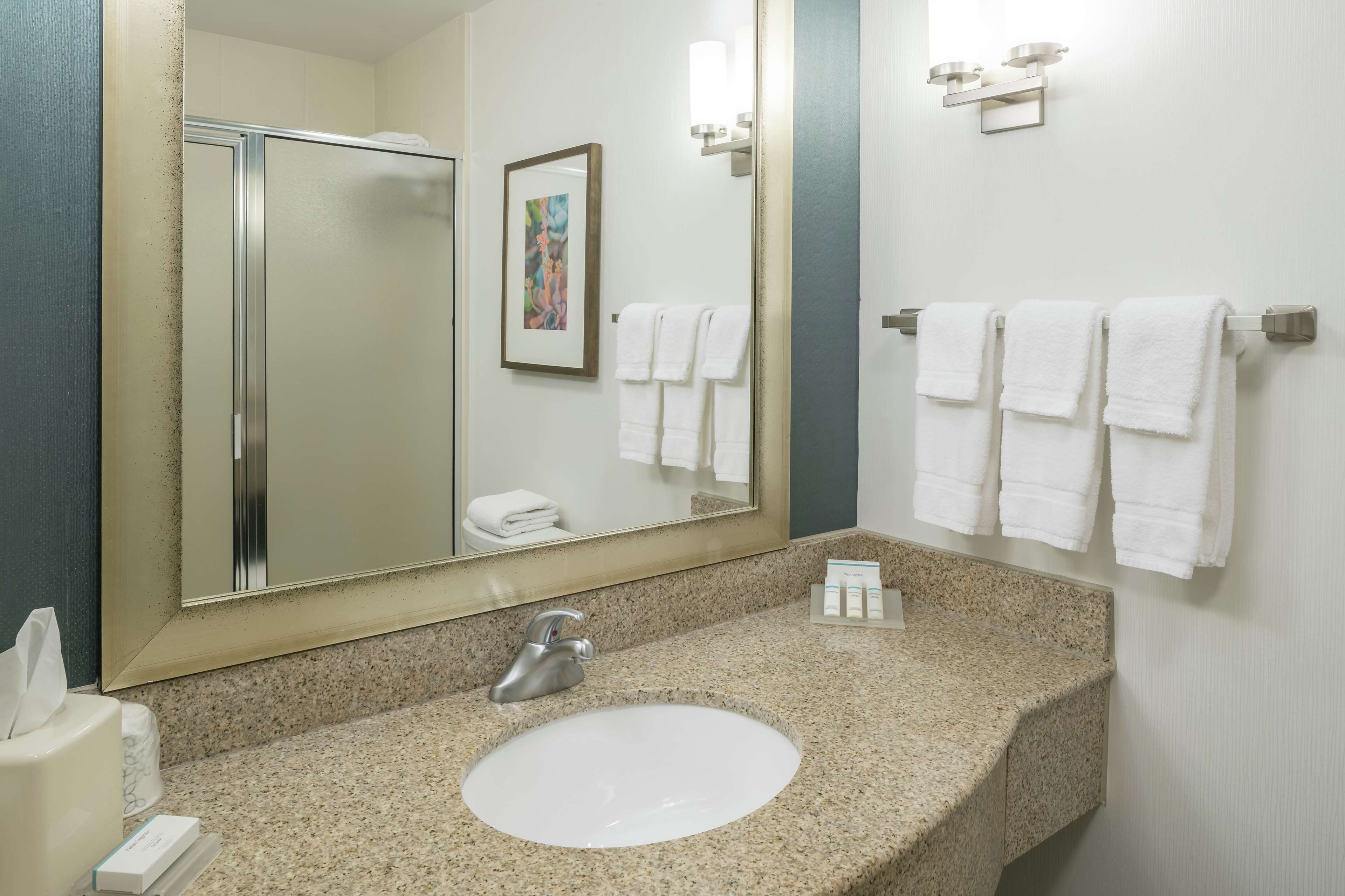 A bathroom with a granite countertop, a white sink, a mirror, and a towel rack with multiple towels.