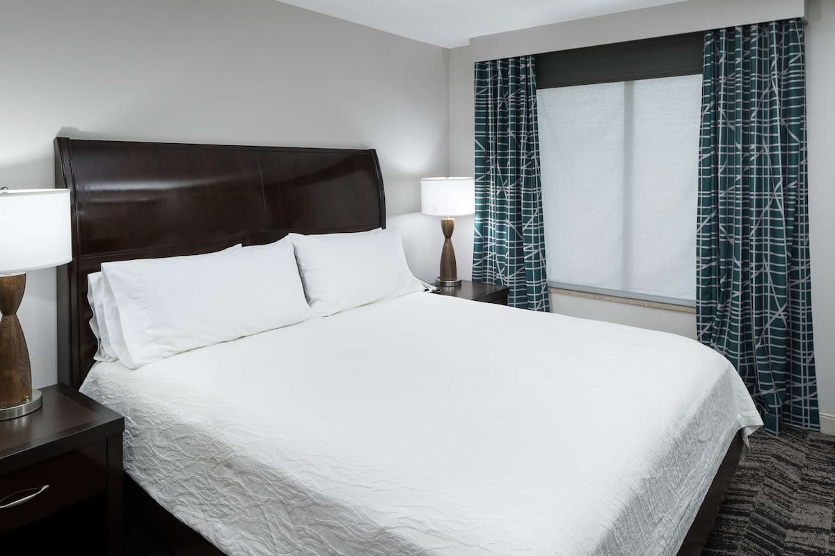 A neatly made bed with white linens, a dark headboard, and two bedside lamps.