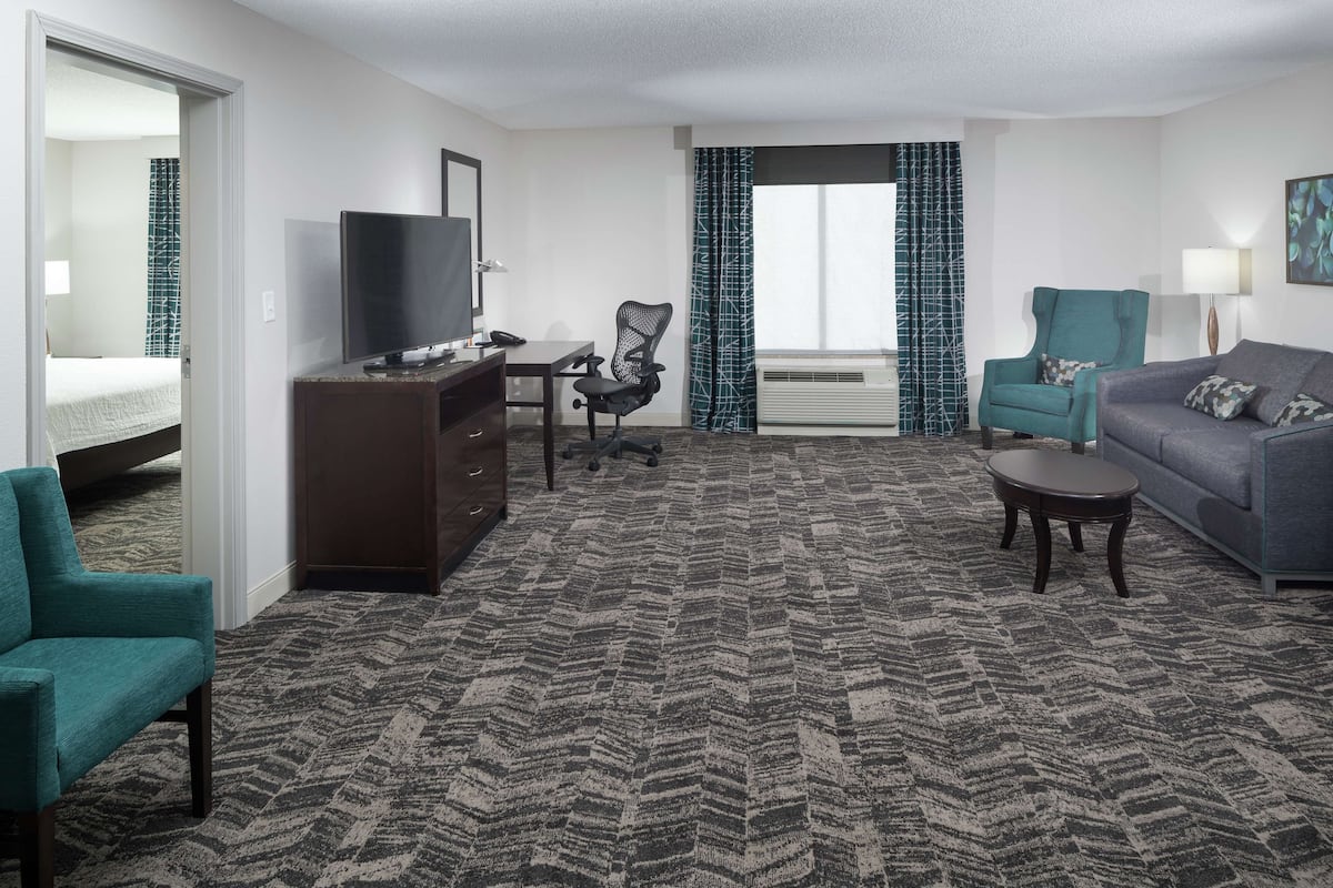 A hotel room with a bed, a desk with a TV, a sofa, a chair, and a carpeted floor.