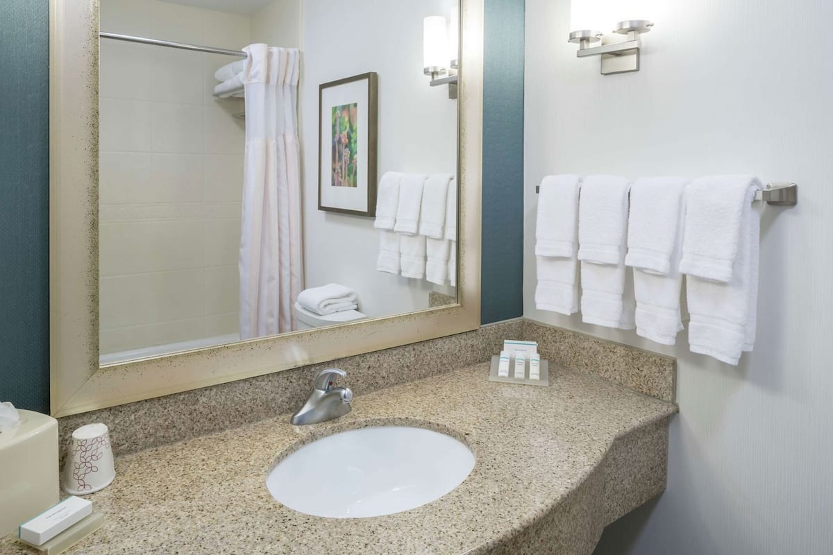 A bathroom with a granite countertop, a white sink, a large mirror, a shower curtain, and multiple white towels.