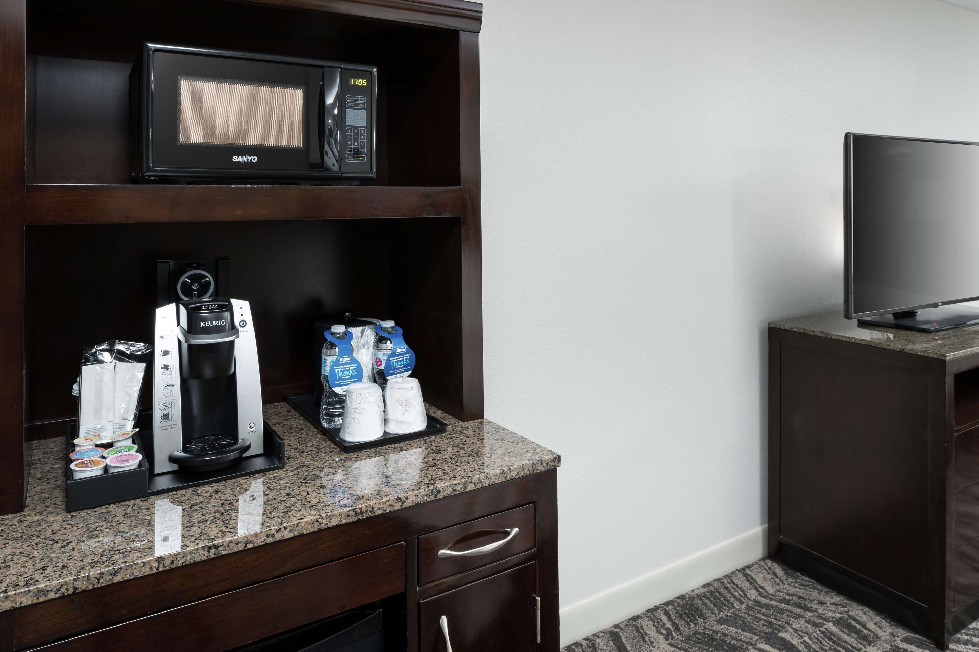 A hotel room with a microwave, coffee maker, and bottled water on the counter.