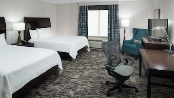 A hotel room with two beds, a desk, a chair, a TV, and a window with curtains.