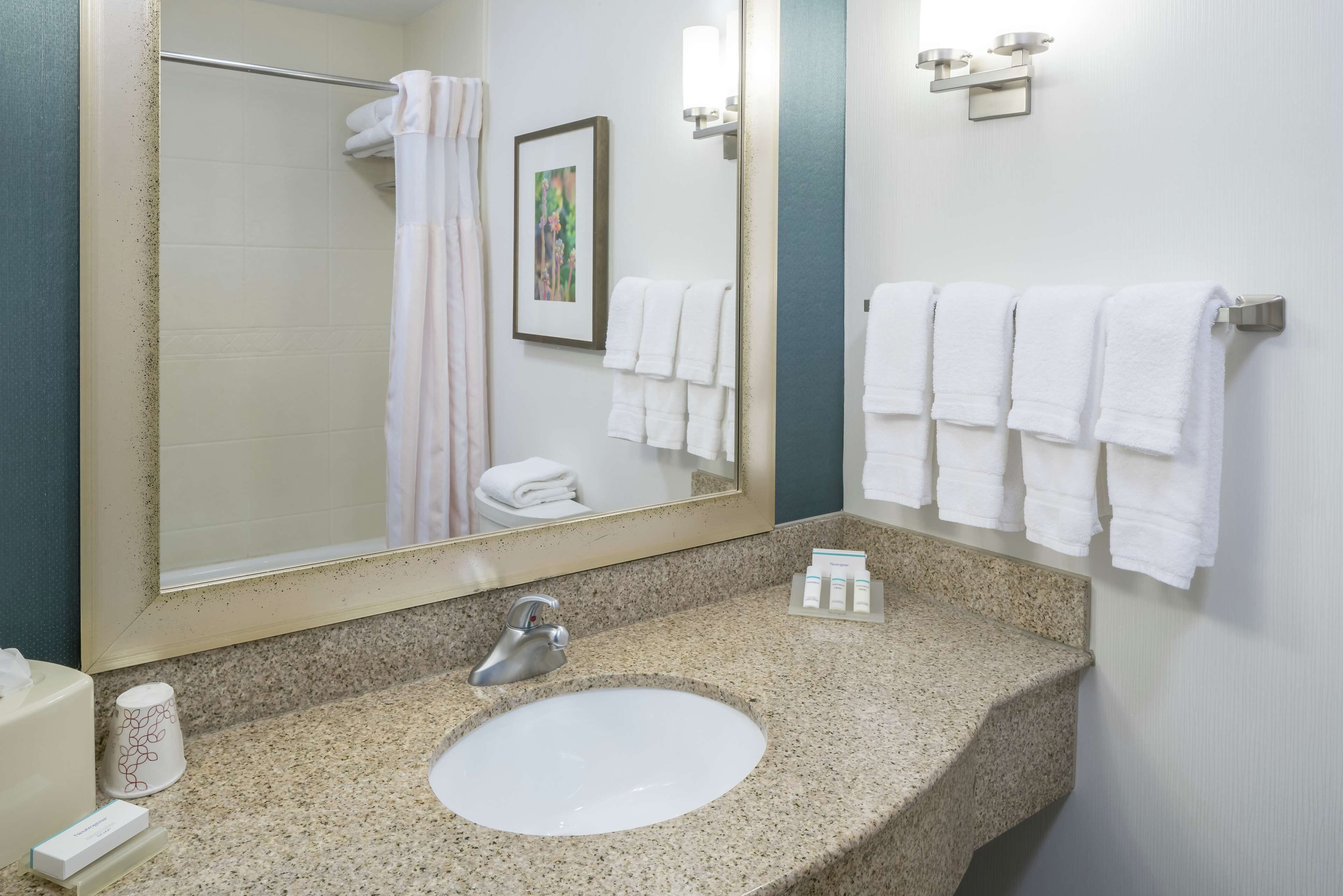 A bathroom with a granite countertop, a white sink, a large mirror, and multiple white towels hanging on the wall.