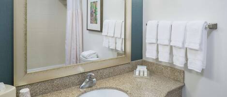 A bathroom with a granite countertop, a white sink, a large mirror, and multiple white towels hanging on the wall.