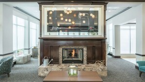 A modern lobby with a fireplace, seating area, and a large window with a view. - Hilton Garden Inn Dothan (Dothan)