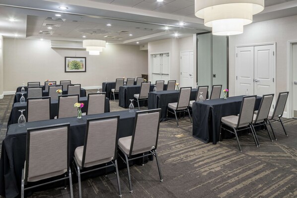 Un salón de conferencias con varias mesas y sillas, equipado con vasos de agua y jarrones.