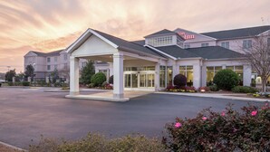 A hotel with a covered entrance, a parking lot, and a landscaped area with flowers. - Hilton Garden Inn Dothan (Dothan)