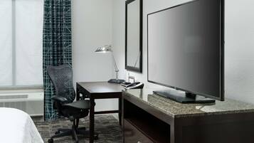 A hotel room with a bed, a desk with a computer, a TV, a lamp, and a chair.