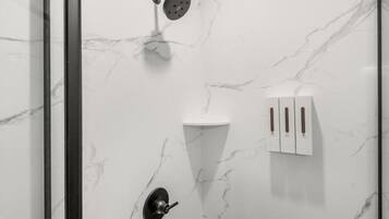 A modern bathroom with a shower, a sink, and a soap dispenser.