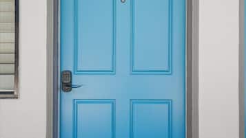 Una puerta azul con cerradura electrónica, un ventanal con persianas y una pared blanca.