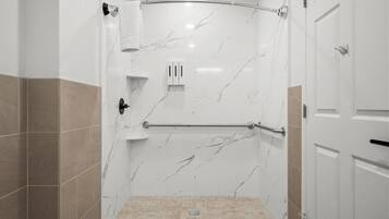 A walk-in shower with a curved showerhead, a towel rack, and a handrail.