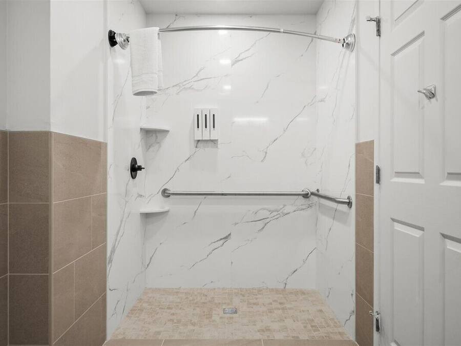 A walk-in shower with a curved showerhead, a towel rack, and a handrail.