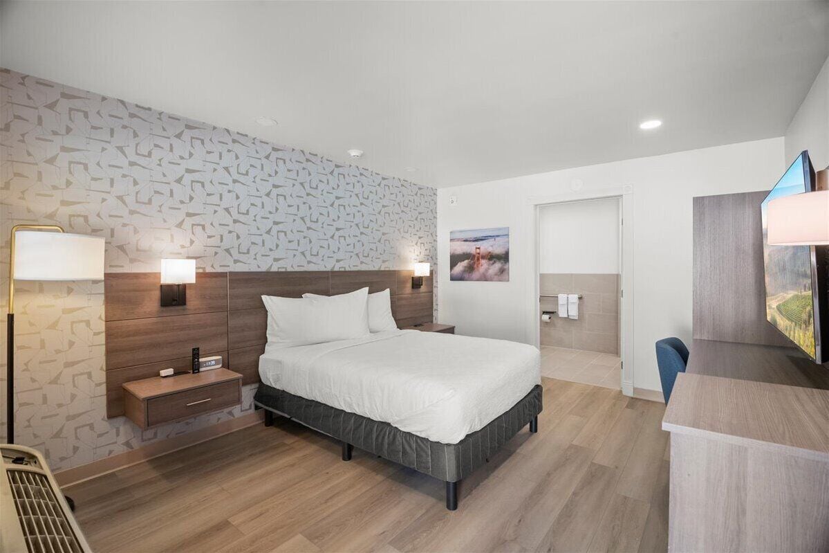 Moderni hotellihuone, jossa on suuri sänky, yöpöydällä olevat lamput, työpöytä ja televisio.