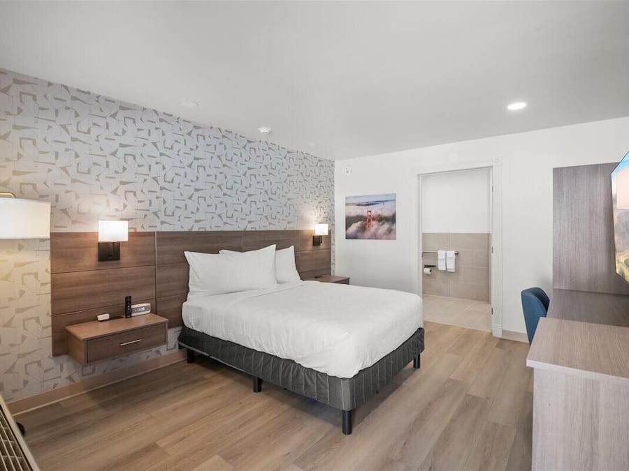A modern hotel room with a large bed, bedside lamps, a desk, and a TV.