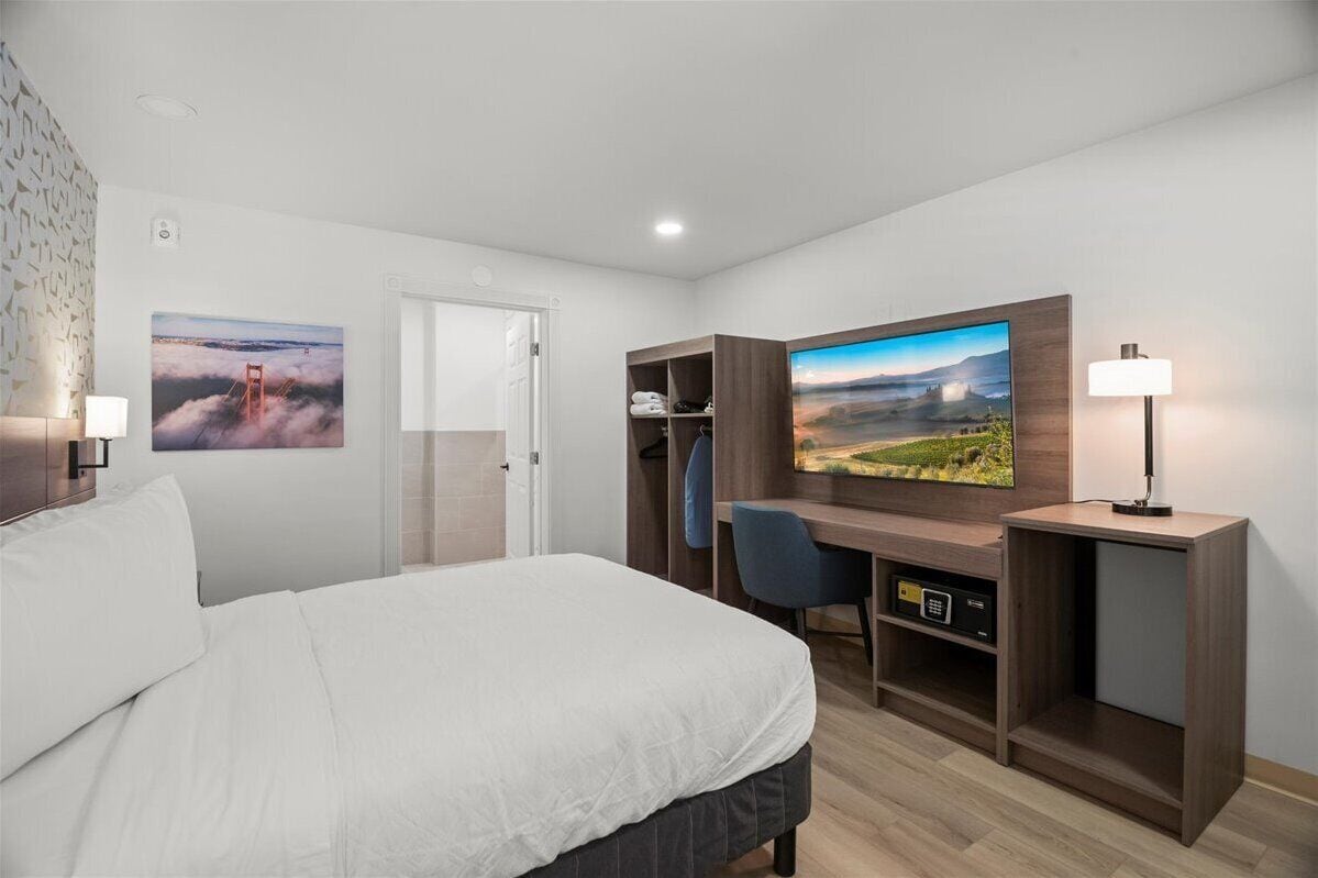 A hotel room with a bed, a desk, a chair, a TV, and a wardrobe.