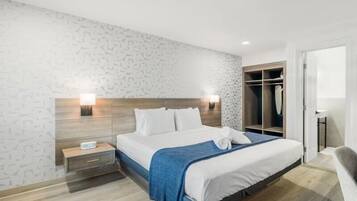 Una habitación de hotel moderna con una cama grande, lámparas de noche, cabecera de madera, vestidor y baño con inodoro y lavabo.