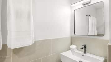 Un baño moderno con un lavamanos blanco, un espejo y una toalla colgada en la pared.