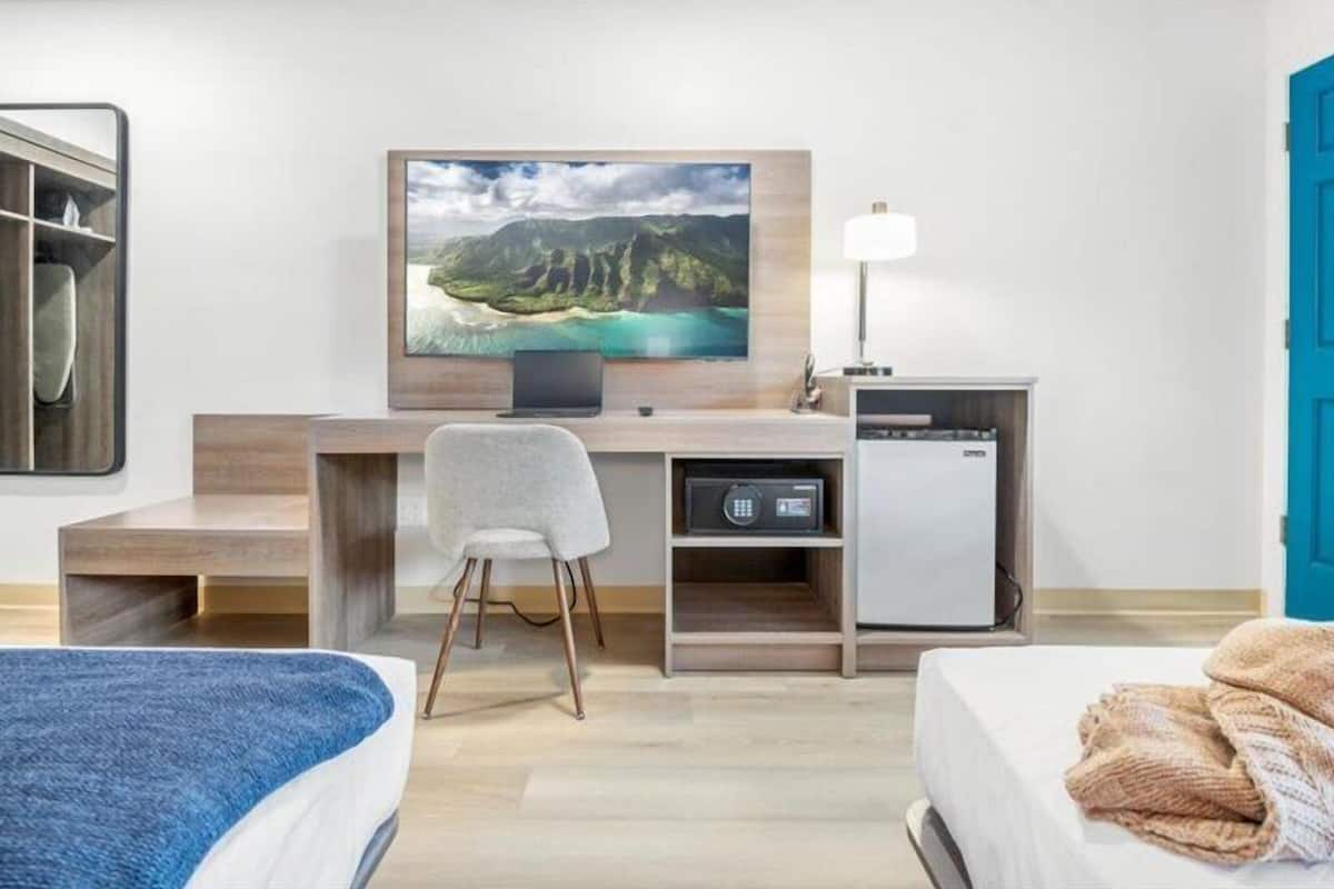 A hotel room with a bed, a desk with a computer, a television, and a small refrigerator.