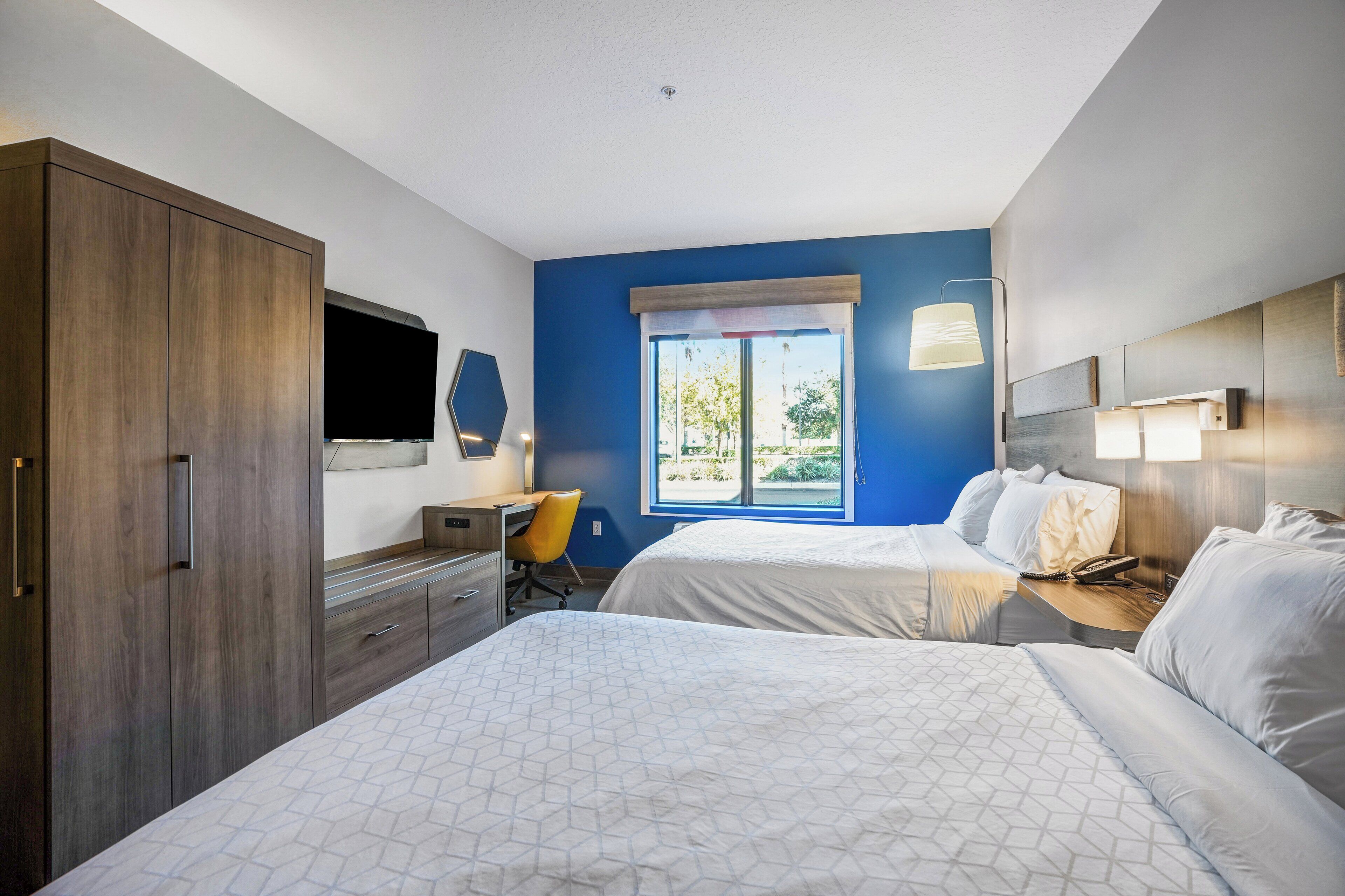 Hotellihuone, jossa on kaksi sänkyä, työpöytä, tuoli, televisio ja ikkuna, josta on näkymä.