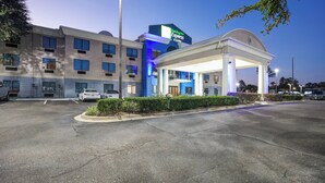 Un hotel Holiday Inn Express & Suites con una entrada bien iluminada, estacionamiento y un área exterior techada.