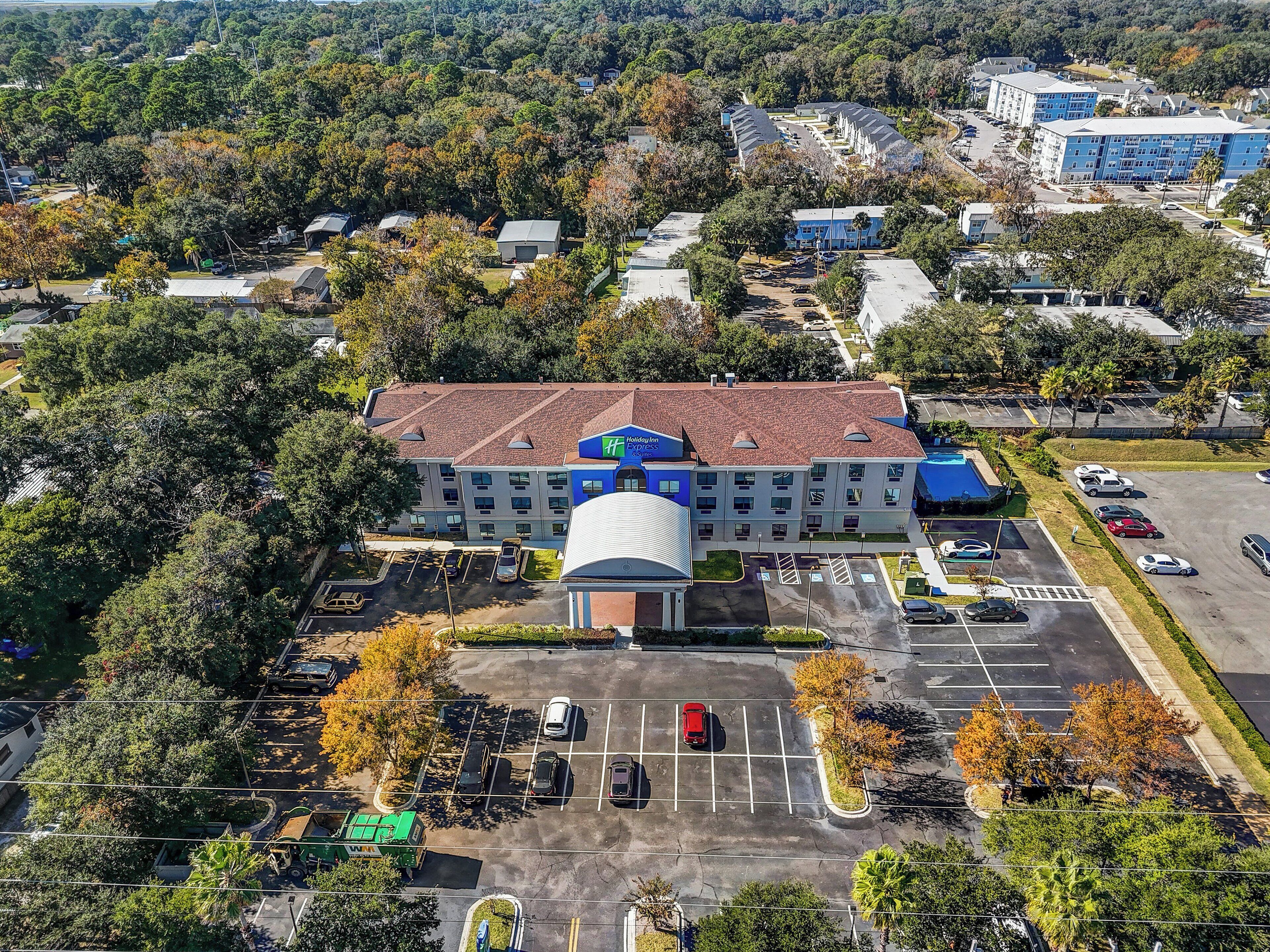 An aerial view of a Holiday Inn Express hotel with a parking lot, surrounded by trees and other buildings.