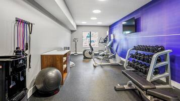 Un gimnasio con equipo de ejercicio, dispensador de agua y una televisión instalada en la pared.