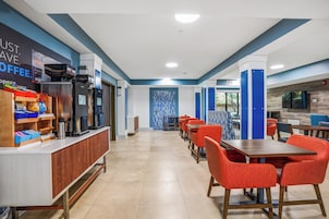 Un moderno vestíbulo de hotel con una larga recepción, sillas rojas y una cafetería.