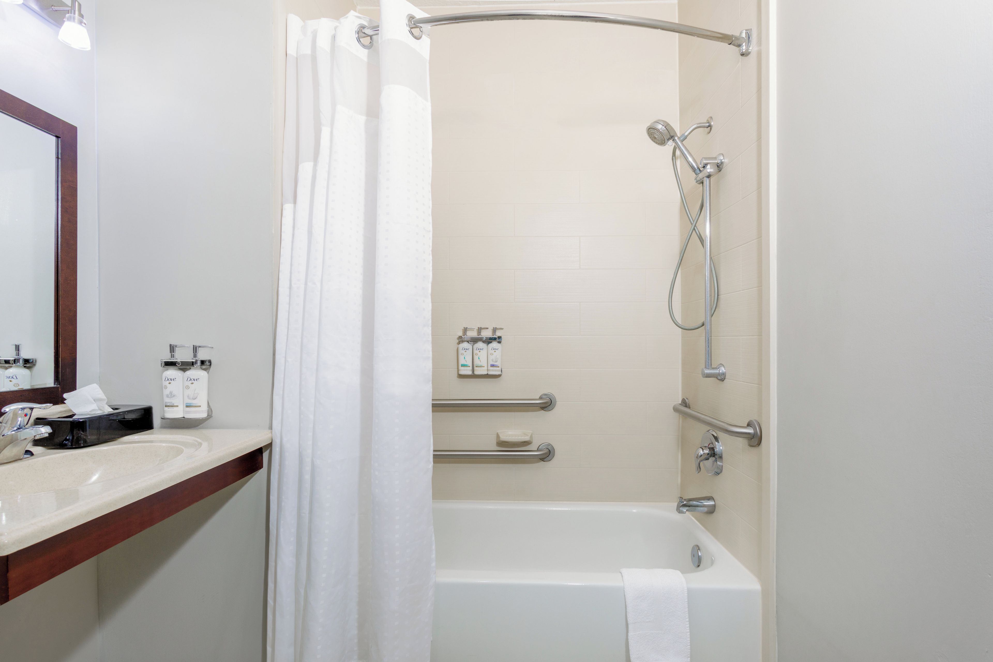 A bathroom with a bathtub, shower, and a vanity with a mirror and toiletries.