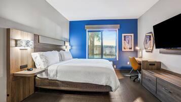 A modern bedroom with a bed, bedside table, desk, chair, and a large window with a view.