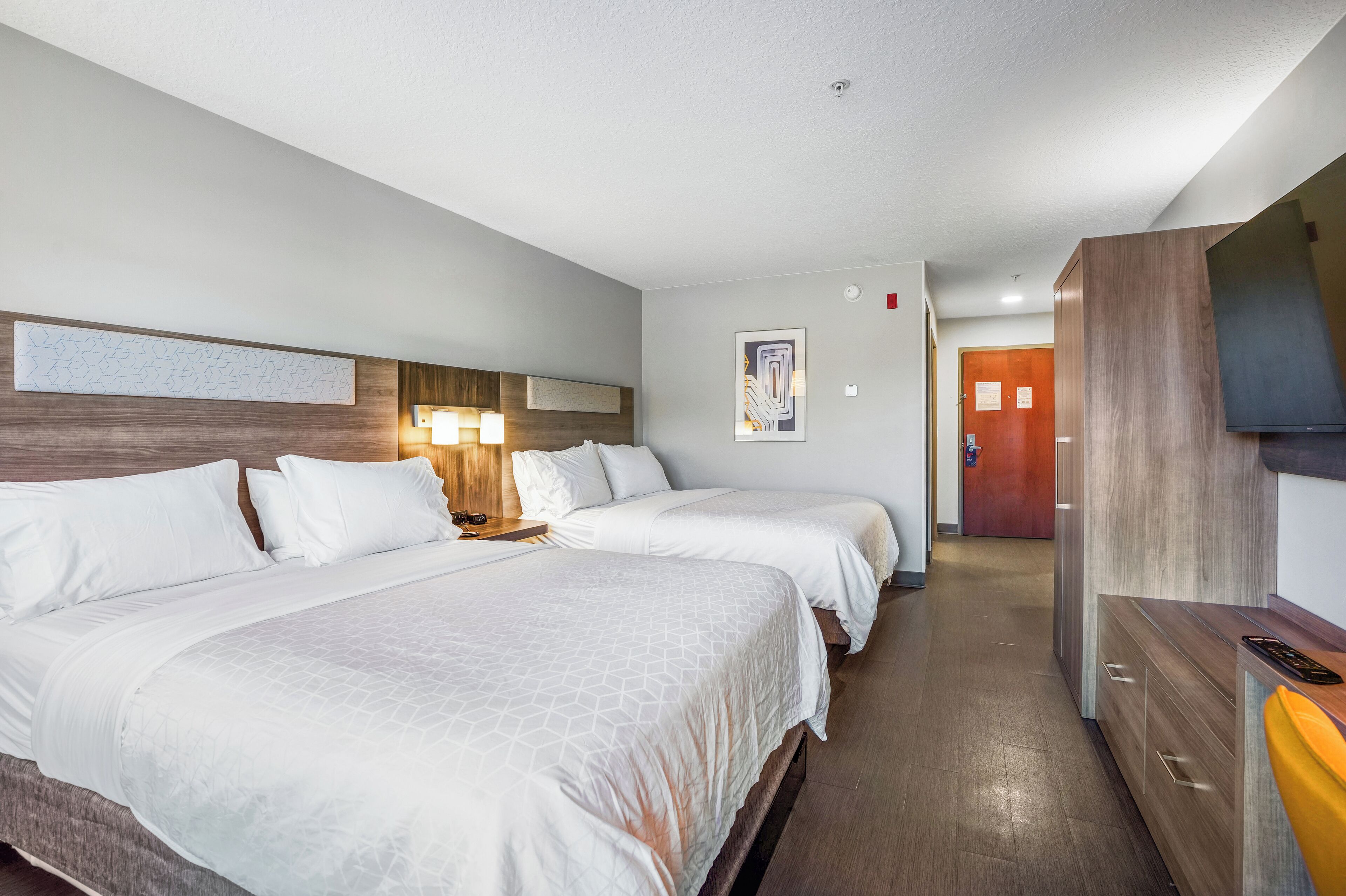 Habitación de hotel con dos camas, cabecera de madera, televisión de pantalla plana y cómoda de madera.