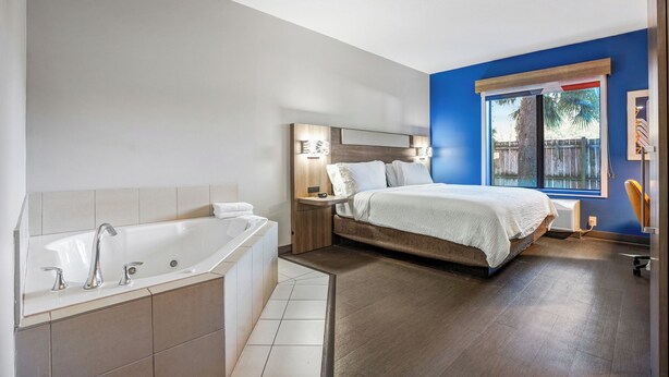 Un dormitorio moderno con una cama grande, cabecero integrado y ventana con vista a palmeras.