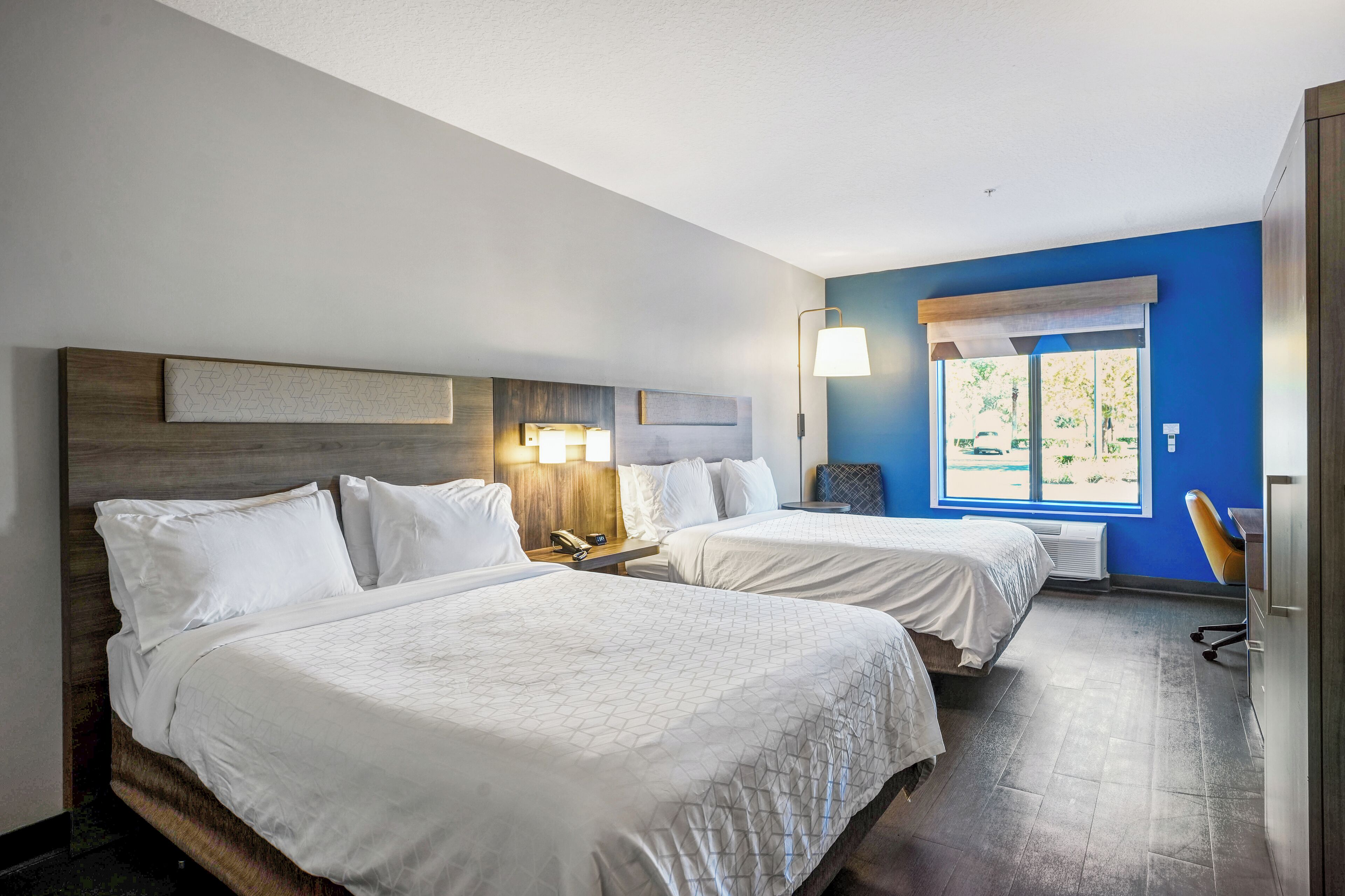 Hotellihuone, jossa on kaksi sänkyä, yöpöytä, lamppu, ikkuna, josta on näkymä, ja tuoli.