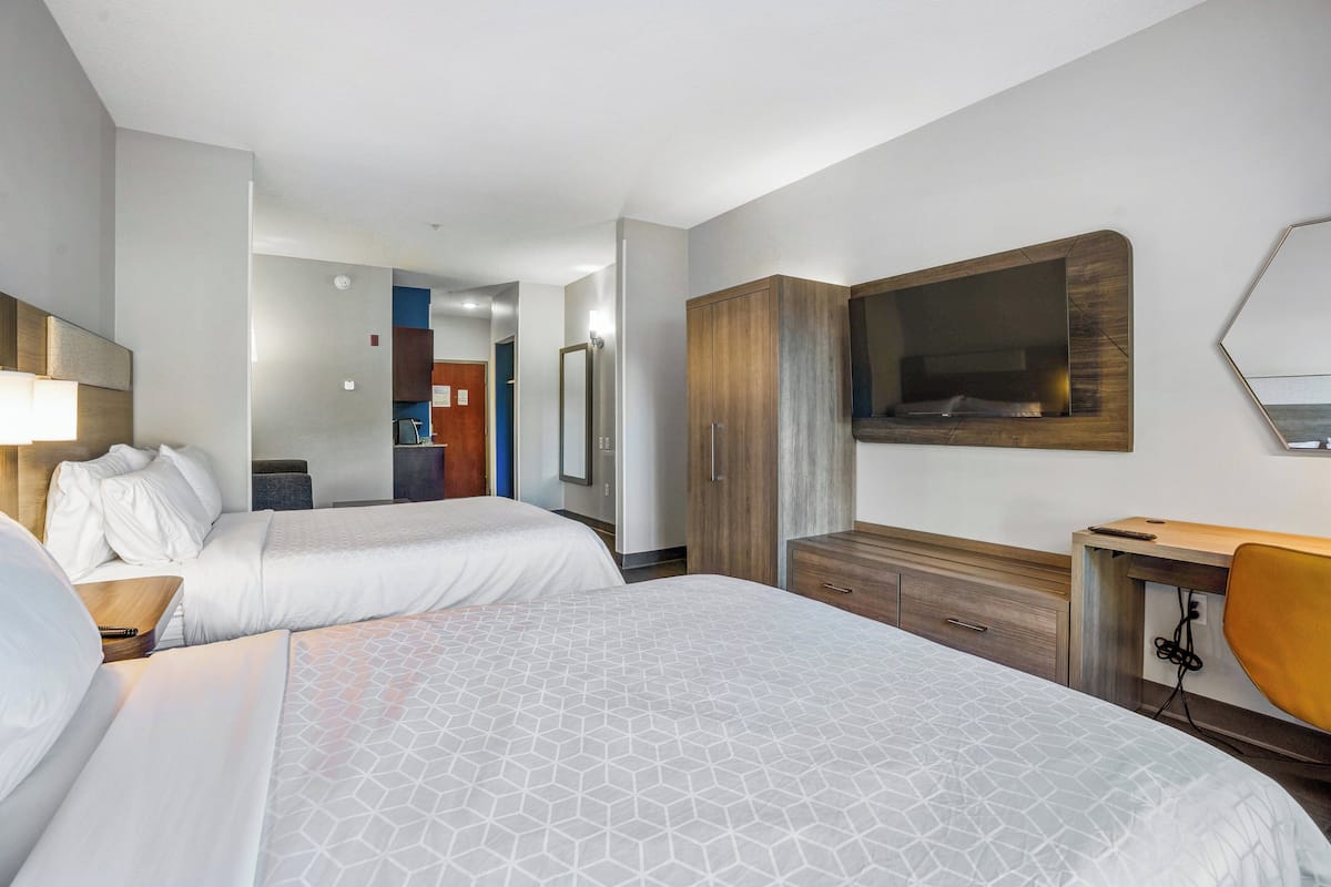 Een hotelkamer met twee bedden, een houten garderobe, een bureau met stoel, en een grote spiegel aan de muur.