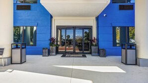 Una entrada de edificio moderna con fachada azul, amplias puertas de vidrio y un vestíbulo cubierto.