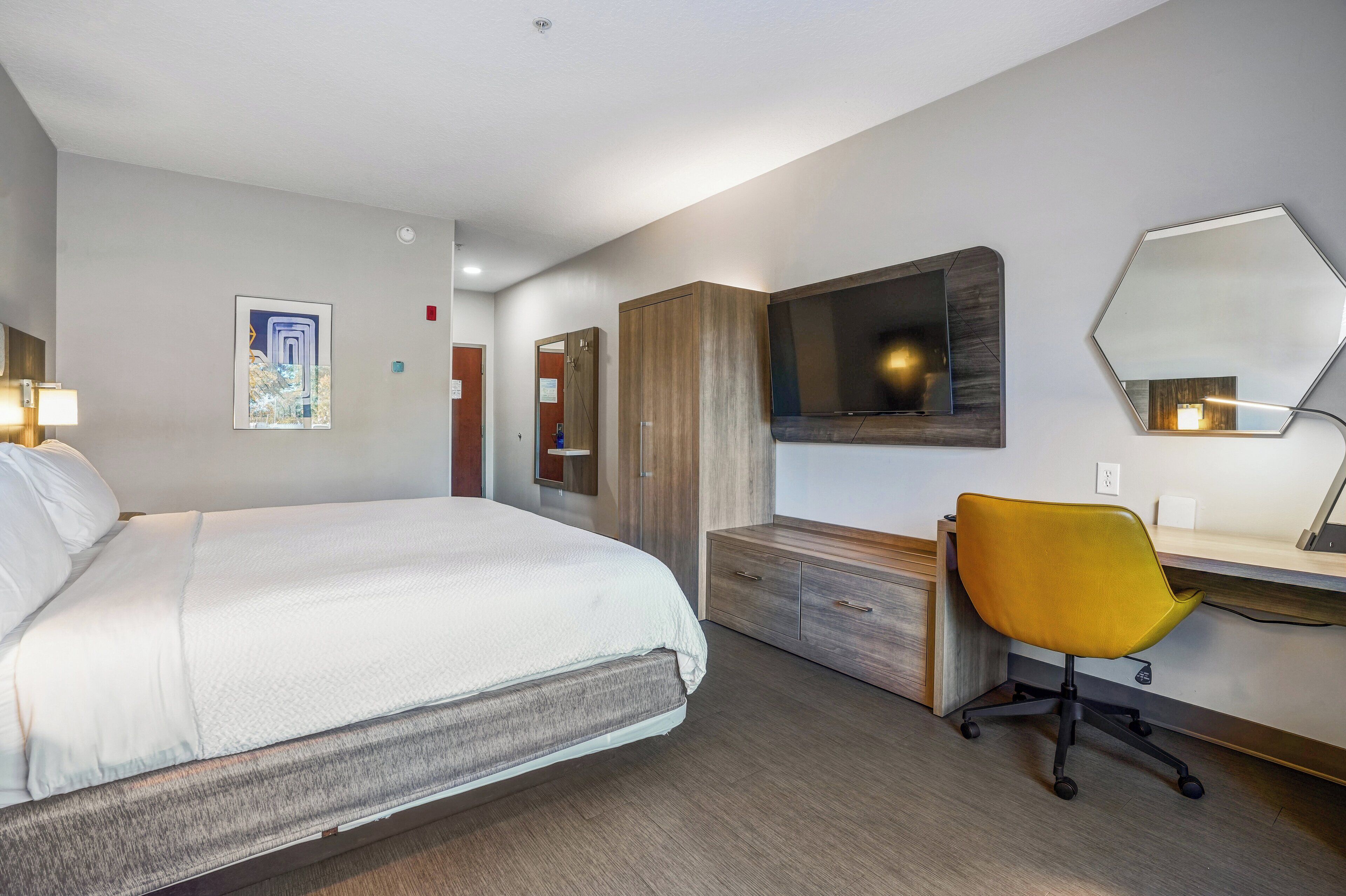 Een hotelkamer met een bed, bureau, stoel, televisie en spiegel.