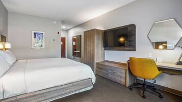 Een hotelkamer met een bed, bureau, stoel, televisie en spiegel.