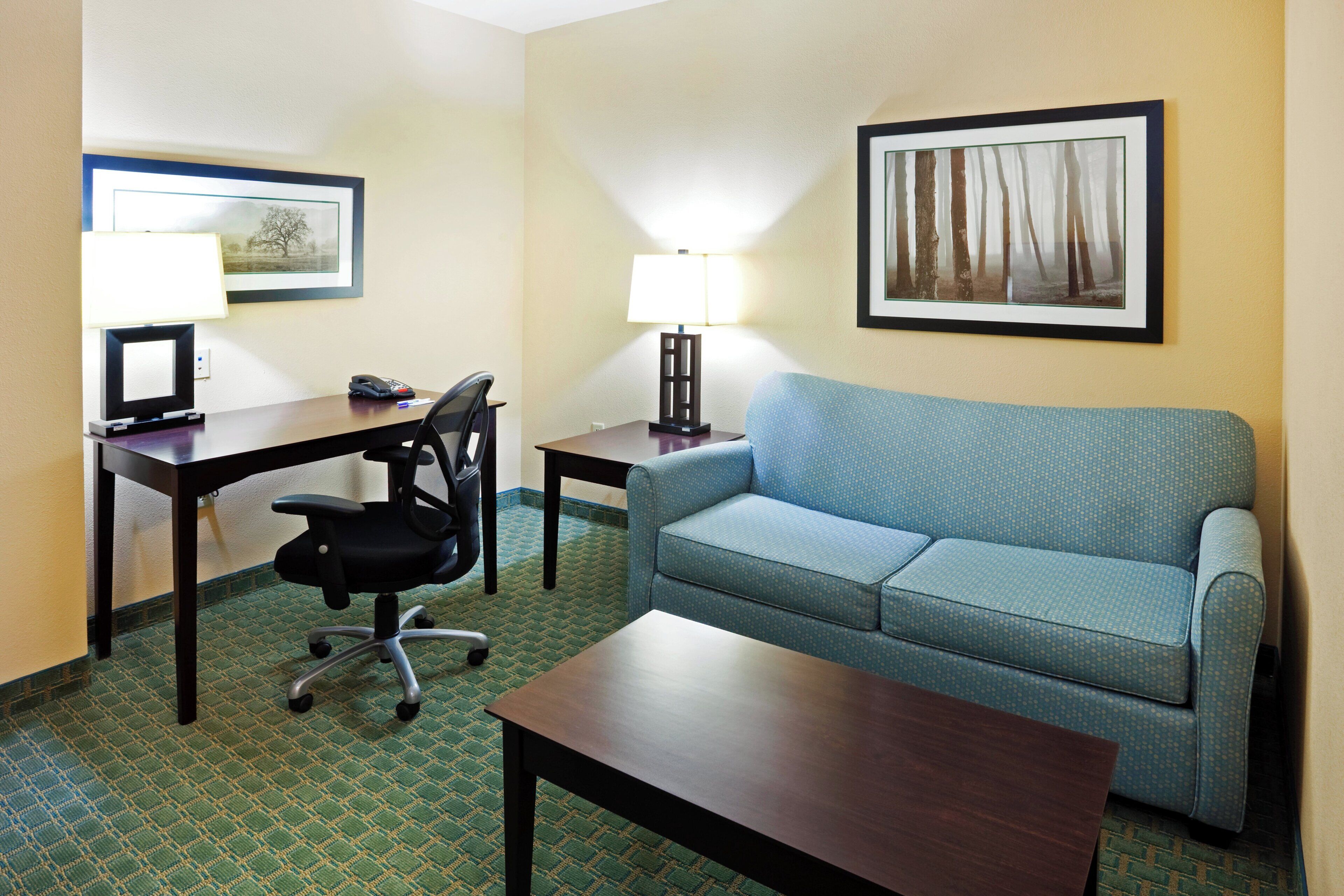 A hotel room with a desk, chair, sofa, and two lamps.