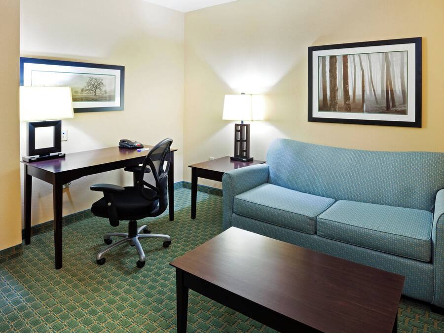 A hotel room with a desk, chair, sofa, and two lamps.