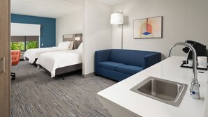 A hotel room with two beds, a blue sofa, a white sink, and a large window. - Holiday Inn Express & Suites Newport S by IHG (Newport)