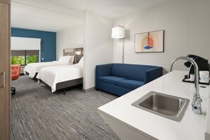 A hotel room with two beds, a blue sofa, a white sink, and a large window. - Holiday Inn Express & Suites Newport S by IHG (Newport)