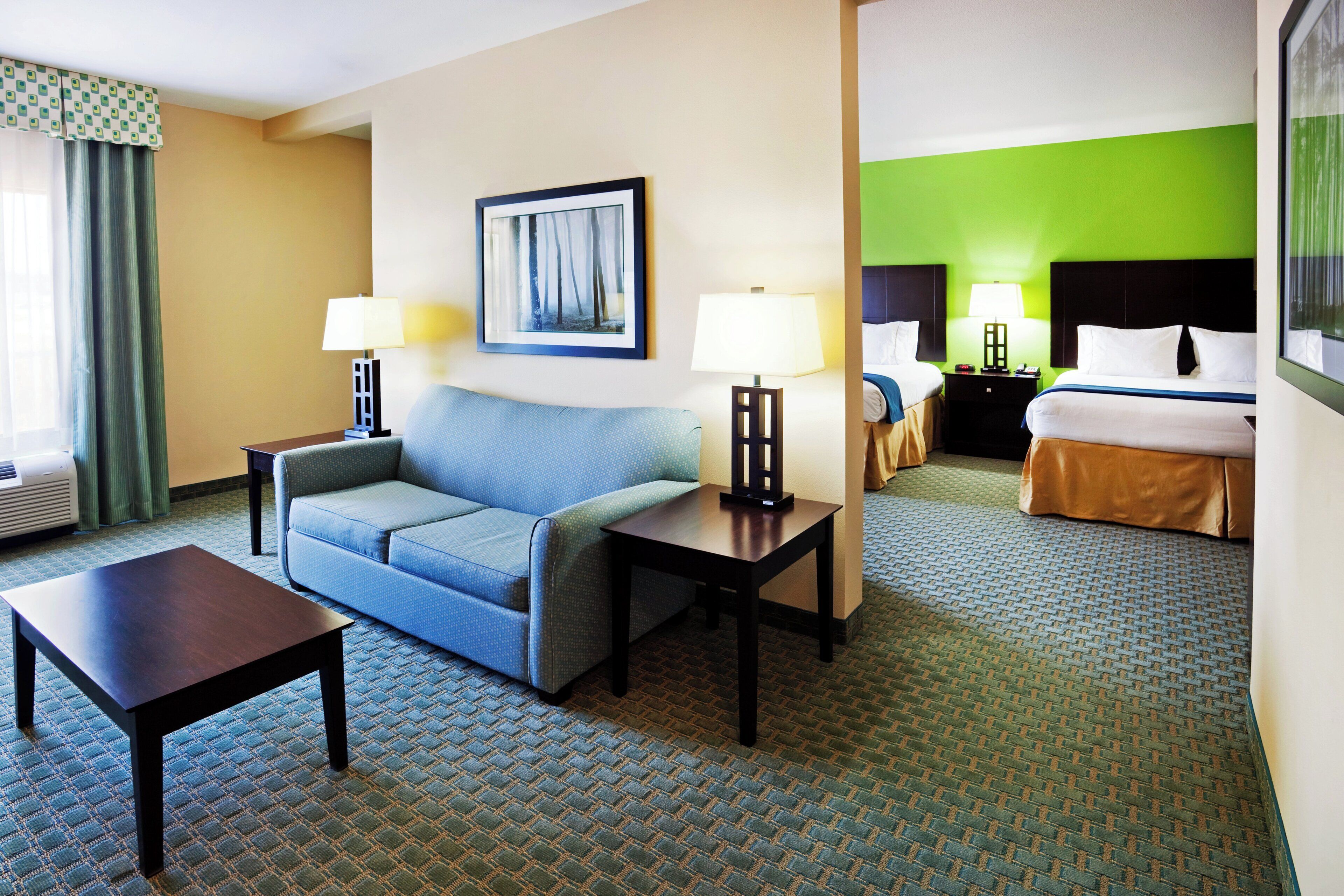 A hotel room with a sofa, a table, a bed, and a nightstand with lamps.