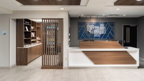 A reception area with a wooden reception desk, a large blue and white geometric wall art, and a wooden bookshelf with various items. - Holiday Inn Express & Suites Newport S by IHG (Newport)