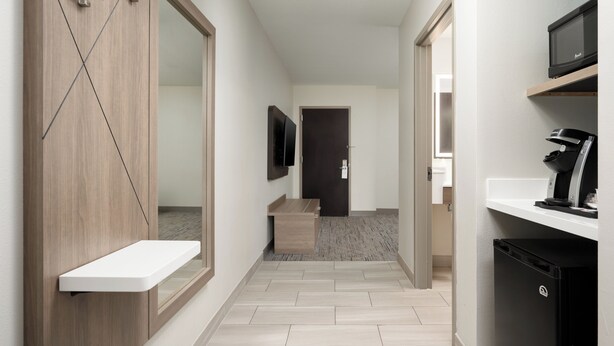 A modern hallway with a wooden wardrobe, a small white shelf, a flat-screen TV, a microwave, and a coffee machine. - Holiday Inn Express & Suites Newport S by IHG (Newport)