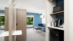 A modern hotel room with a wooden wardrobe, a blue sofa, a coffee machine, and a microwave on a shelf. - Holiday Inn Express & Suites Newport S by IHG (Newport)